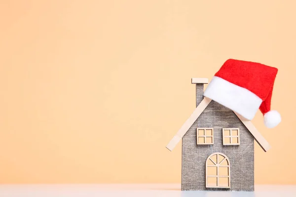 Wooden house model with santa hat on beige background