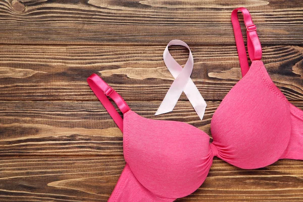 Pink ribbon with female bra on wooden background