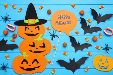 Mavi ahşap arka planda kağıt yarasalar, balkabakları, örümcekler ve şekerler ile Mutlu Cadılar Bayramı metni