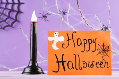 Mutlu Cadılar Bayramı 'nı mum, ağaç dalları ve mor arkaplandaki örümceklerle kutlayın.