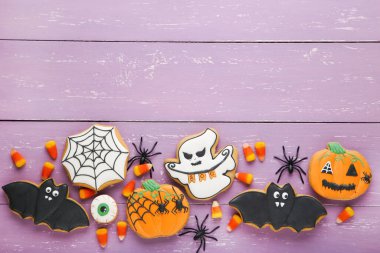 Cadılar Bayramı zencefilli kurabiyeler ve mor ahşap masada örümcekler.