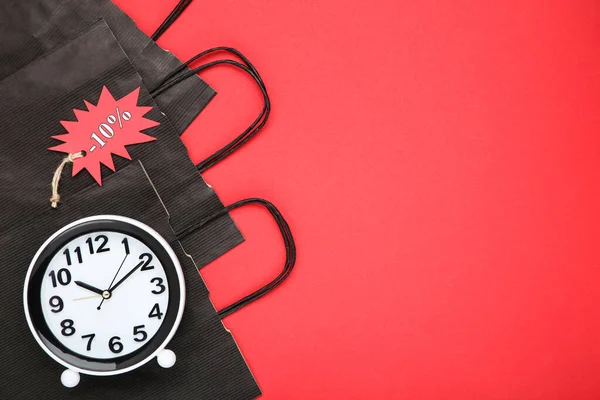 Paper tag, clock and black shopping bags on red background