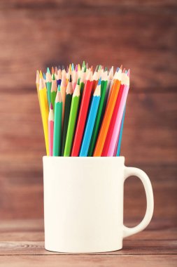 Ahşap masada beyaz fincanda renkli kalemler.