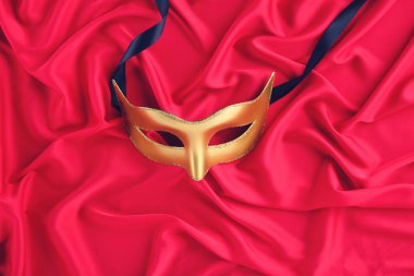 Kırmızı kumaş arka planda kurdeleli karnaval maskesi
