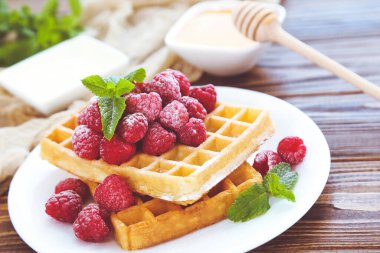 Taze ahududu ve kahverengi ahşap arka planda nane yapraklı lezzetli waffle 'lar.