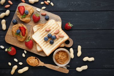 Fıstık ezmeli ekmek, siyah ahşap masada meyve ve fındık.