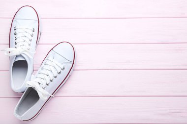 Pembe tahta masada bir çift beyaz spor ayakkabı.