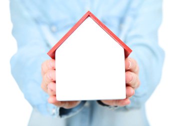 Ahşap ev modeli ve aileyi tutan kadın elleri.