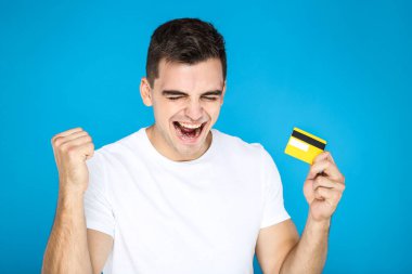 Genç mutlu adam mavi arka planda kredi kartı tutuyor.