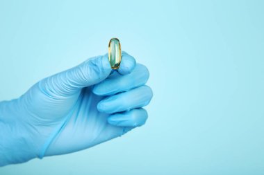 Eldivenli doktor mavi arka planda kapsülü tutuyor.