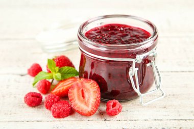 Cam kavanozda tatlı ahududu reçeli ve beyaz ahşap masada olgun böğürtlen.