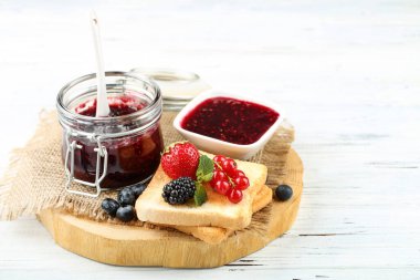 Kavanozda reçel, cam kavanoz ve beyaz ahşap masada böğürtlen.