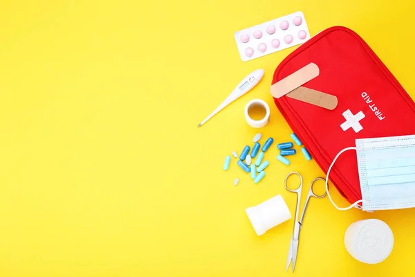 First aid kit with medical supplies on yellow background