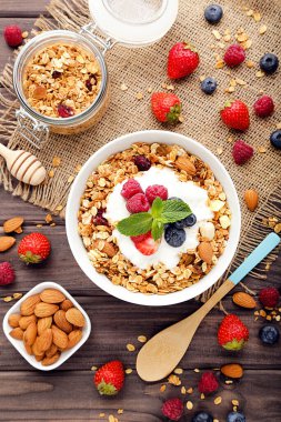 Kahverengi ahşap arka planda taze böğürtlenli ve bademli lezzetli granola.