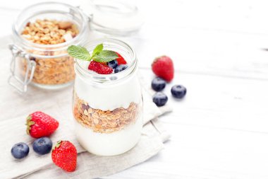 Beyaz ahşap arka planda kremalı ve dutlu lezzetli granola.