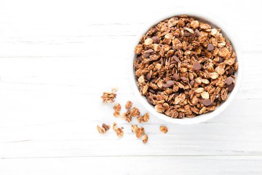 Beyaz ahşap arka planda kasede lezzetli çikolata tanecikleri.