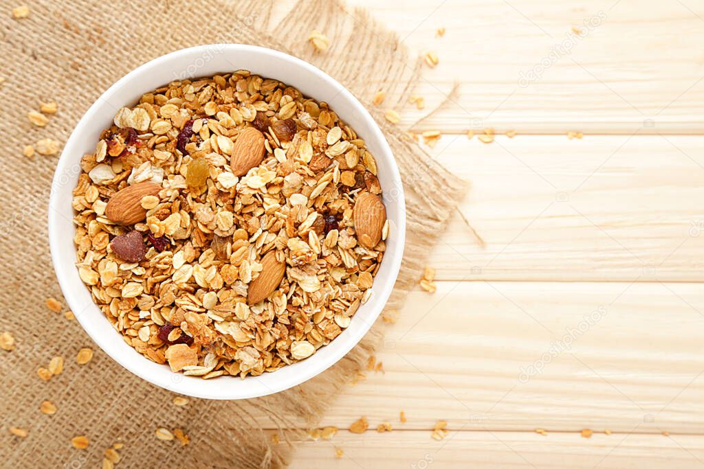 Tasty granola in bowl on brown wooden background