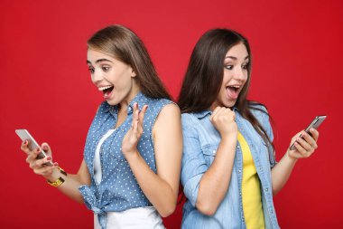 Kırmızı arka planda cep telefonu olan genç kız arkadaşlar
