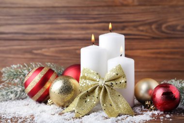 Süslü Noel mumları ve kahverengi ahşap arka planda beyaz kar.