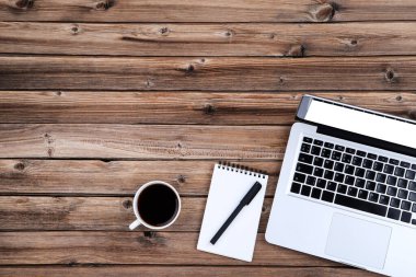 Kahverengi ahşap masada bir fincan kahve ve not defteri olan dizüstü bilgisayar.