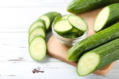 Beyaz ahşap arka planda cam kasede salatalıklar ve dilimler.