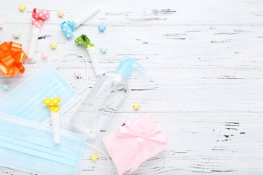 Beyaz ahşap arka planda jel dezenfektanı, hediye kutusu, düdük ve renkli kağıt yıldızlı tıbbi maskeler.