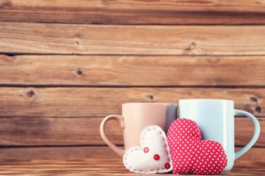 Kahverengi ahşap masada fincanlı kumaş kalpler.