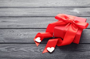 Kurdeleli hediye kutusu ve siyah ahşap masada kalpler.