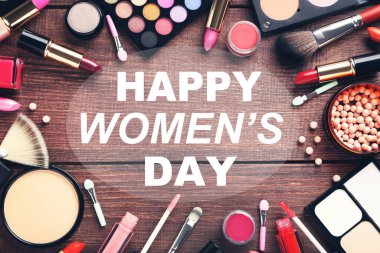 Different makeup cosmetics with text Happy Womens Day on brown wooden table