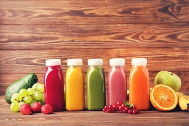 Kahverengi ahşap arka planda meyve ve sebzeli plastik şişelerde meyve püresi