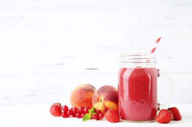 Beyaz ahşap arka planda meyveli cam kavanozda kırmızı smoothie.