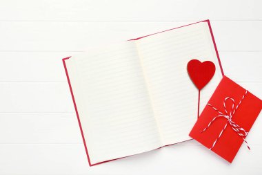 Kırmızı kalpli kağıt zarf ve beyaz ahşap masa üzerinde not defteri.