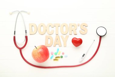 Beyaz ahşap masada termometre, renkli haplar ve steteskopla Doktorlar Günü 'nü yaz.