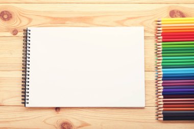 Kahverengi ahşap masa üzerinde defter olan renkli kalemler.