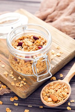 Cam kavanozda lezzetli granola ve kahverengi ahşap arka planda kaşık.