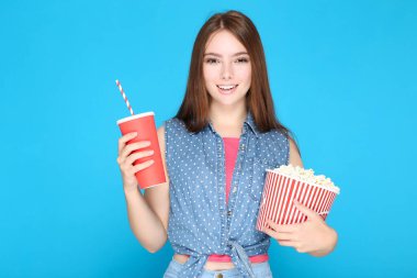 Mavi arka planda patlamış mısır ve içki dolu güzel bir kız.