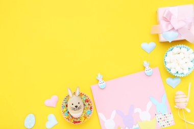 Paskalya konsepti. Hediye kutulu tebrik kartı, marşmelov ve sarı arka planda renkli şekerlemeler.