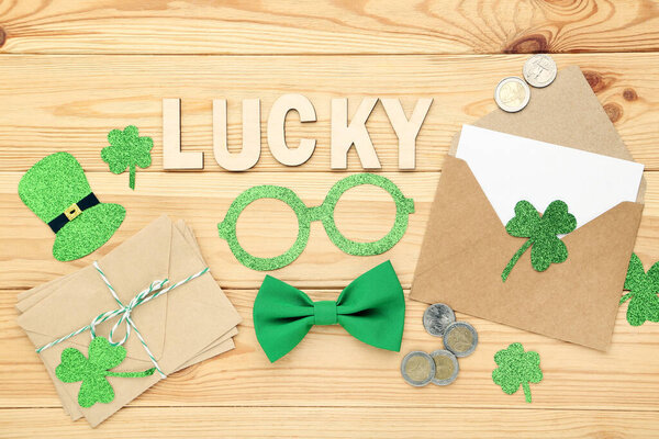 День Святого Патрика. Бумажные листья клевера с конвертами, очками и словом Счастливчик на коричневом деревянном столе