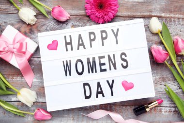 Lale ve Gerbera çiçekleri, mesajlı ışık kutusu Mutlu Kadınlar Günü, hediye kutusu ve tahta arka planda ruj.