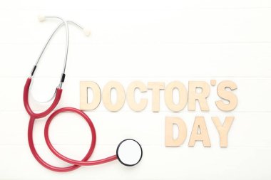 Beyaz ahşap masadaki Doktor Günü yazılı steteskop.