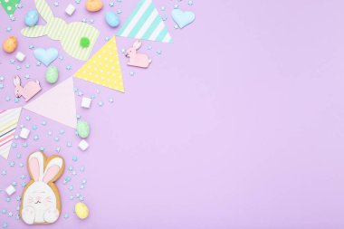 Paskalya konsepti. Tavşanlı kağıt bayraklar, yumurtalar ve mor arkaplanlı serpiştirmeler.
