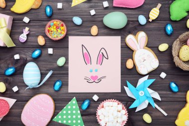 Paskalya zencefilli kurabiyeler, tebrik kartı, yumurta, çikolata ve kahverengi ahşap masada kağıt yel değirmeni.