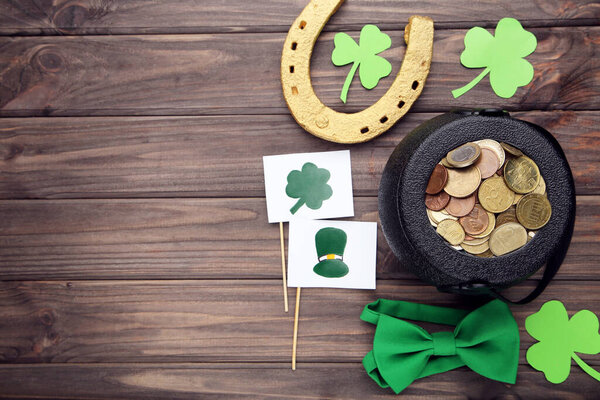 Горшок с монетами с золотой подковой, листьями клевера, галстуком-бабочкой и флагами с изображениями на коричневом деревянном фоне. Концепция Дня Святого Патрика.