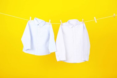 Bebek kıyafetleri sarı arka planda asılı.