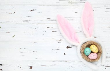 Yuvasında beyaz ahşap arka planda tavşan kulakları olan Paskalya yumurtaları