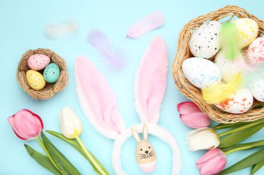 Sepette ve yuvasında lale çiçekleri, tüyler ve mavi arka planda tavşan kulakları olan Paskalya yumurtaları.
