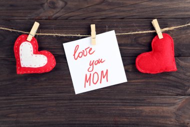 Kahverengi ahşap arka planda asılı kumaş kalplerle seni seviyorum anne.