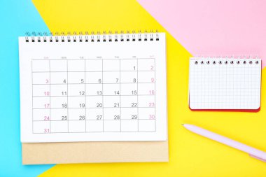 Renkli kağıt arkaplan üzerinde not defteri ve kalemle takvim sayfası