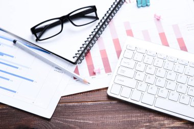 Kahverengi ahşap masa üzerinde diyagramlar ve gözlüklü bilgisayar klavyesi