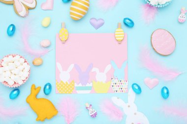 Paskalya konsepti. Kurabiye, yumurta, makarna ve mavi arka planda pembe tüylü tebrik kartı.